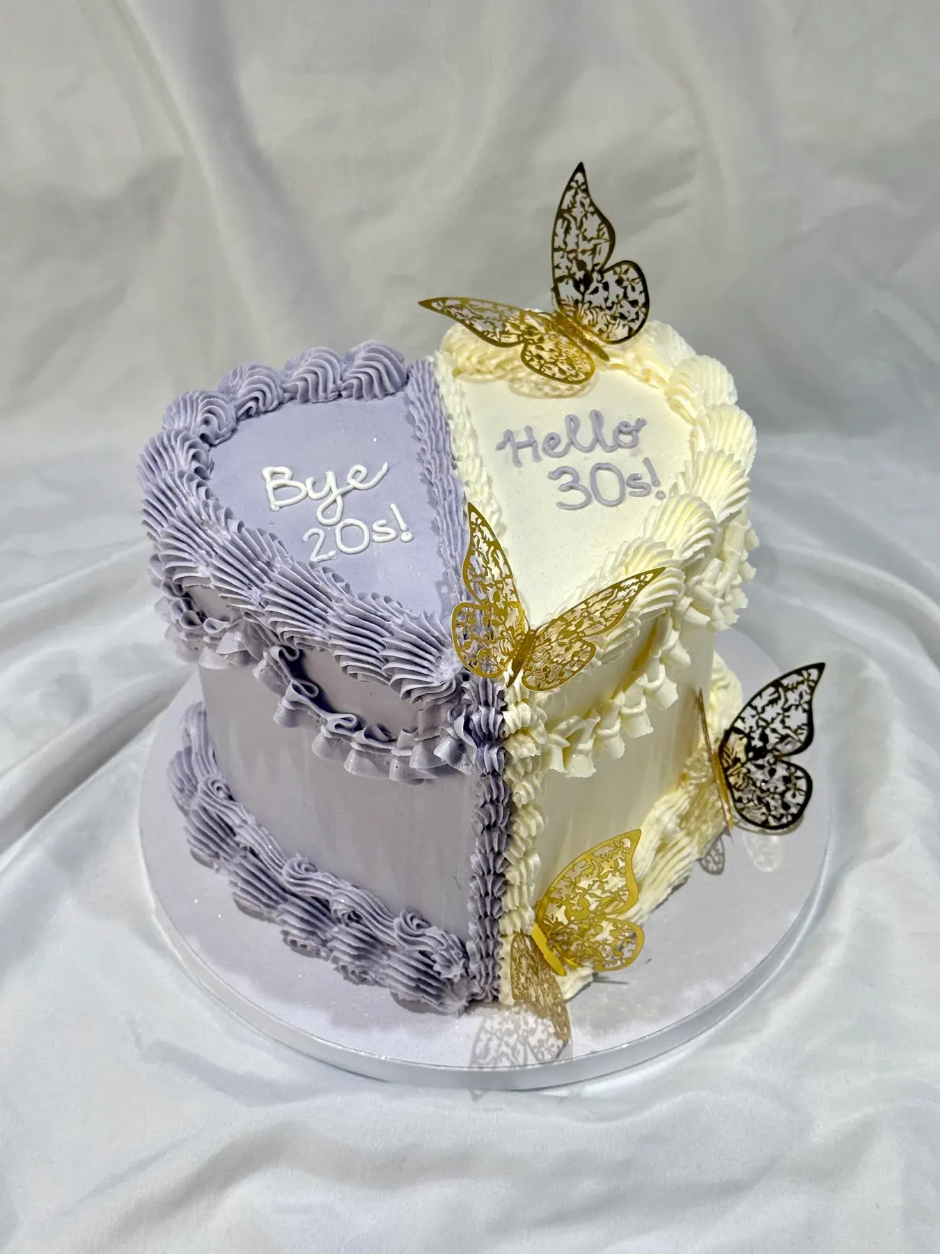 Two-sided heart cake, lilac on one half and gold on the other, reading Bye 20s and Hello 30s, with gold butterflies