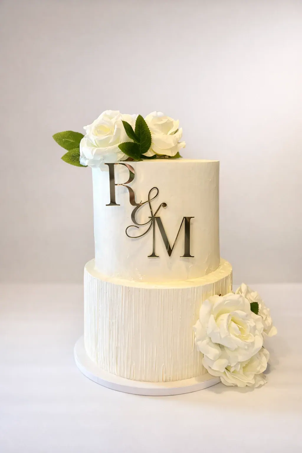 Two-tier ivory wedding cake with a gold R and M monogram and white roses