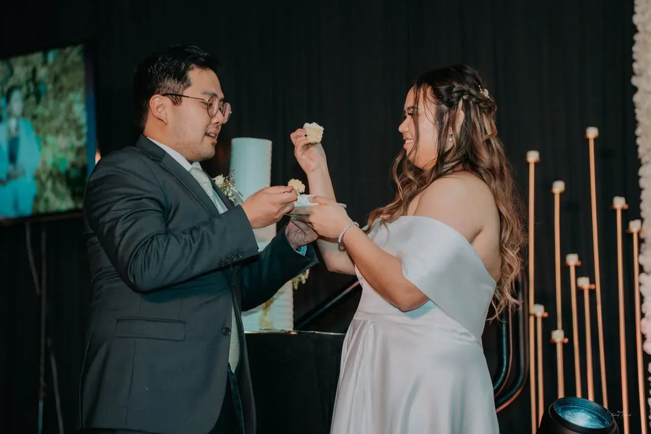 Newlyweds feeding each other a first bite of their Nicsdelite wedding cake at their reception