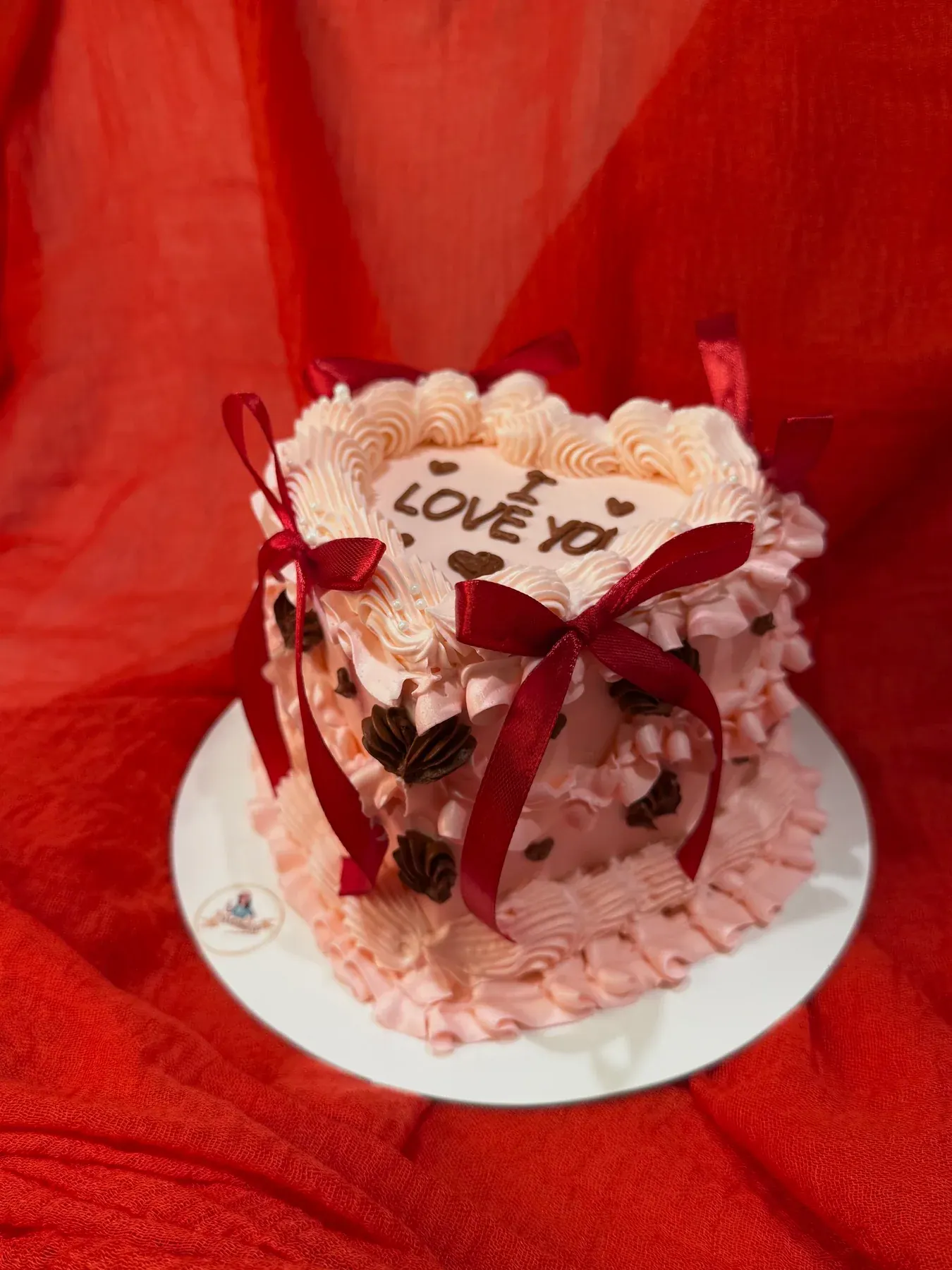 Heart-shaped cake with red piping and a ribbon bow on a red backdrop